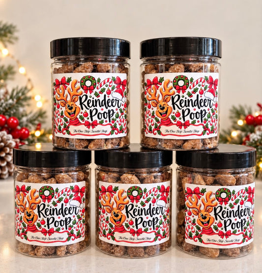 Five clear plastic jars of 'Reindeer Poop' dog treats are arranged in a pyramid on a light surface. The jars have black lids and are decorated with festive labels featuring a cartoon reindeer, red bows, candy canes, and holly.